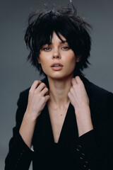Fototapeta premium stylish woman with short black hair posing confidently in black jacket with dark gray background