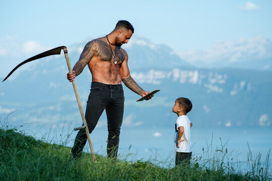 Farmers father and his son work together on field. The father teaches his child how to farm. Father and child on grass farm during harvest. The dad shows his son tablet. Son helps his father on farm.