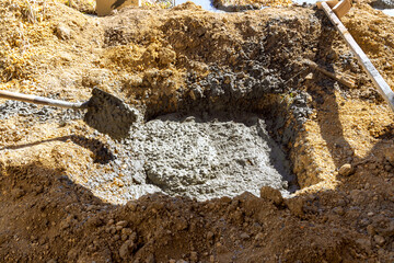 Workers are preparing fresh concrete in large hole at construction site with shovels sand.
