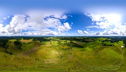 Panoramic aerial view of a landscape. Vast green fields, rolling hills, and scattered trees. Bright, sunny day with puffy white clouds. A network of roads