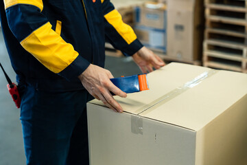Closeup view of logistics staff sealing cardboard box using adhesive tape in warehouse environment...