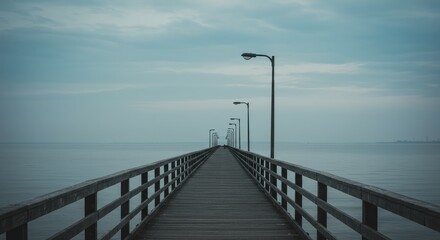 Obraz premium A wooden pier extends into a vast, calm body of water under a muted sky