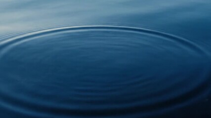 Dramatic abstract background of water drops creating spreading rings on a calm, dark liquid surface