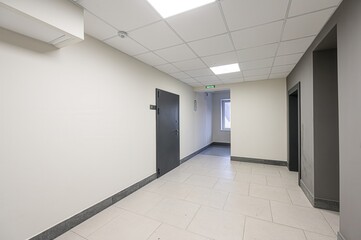 bright, modern corridor with gray doors and a tiled floor. It has an exit sign and a window at the end