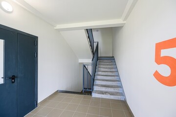 bright entryway features a stairwell with a gray metal railing, tile flooring, a dark blue door, white walls, and a large orange "5"