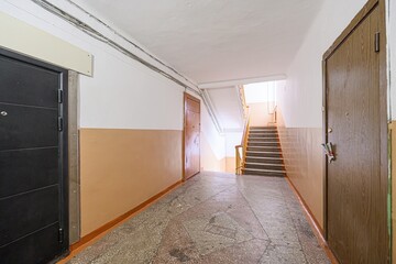 Indoor shot of a hallway featuring two doors, a staircase, and a two-tone wall. The floor is tiled in grey and brown