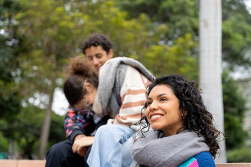 Fototapeta premium Young latin american woman smiling with friends in background in urban park