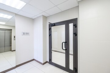 bright, modern interior with white tile walls and floor. Features a glass door and a metal elevator. 