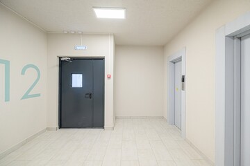 An interior shot featuring an exit door, elevator, light beige walls, and light-colored tiled flooring