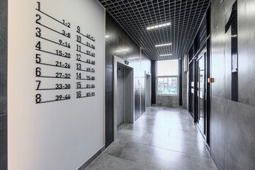 modern, neutral-toned hallway with elevators, a directory sign, and a window at the end of the hall