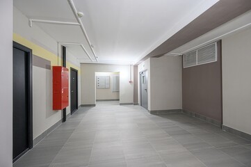 modern hallway interior with neutral walls, gray tiled floor, and black doors.  A red fire hose box adds a pop of color