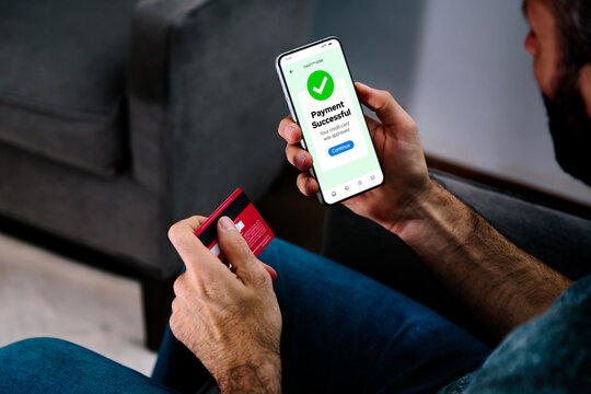 Making a credit or debit card payment online. Successful digital payment confirmation on a mobile phone screen. Man in his living room completing a purchase.