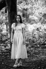 Portrait of a young beautiful dark-haired girl in a dress in the forest. Vintage black and white...
