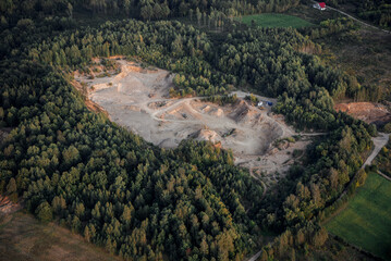 Aerial view of an excavation site surrounded by dense forest showing signs of mining activity at...