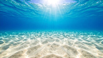 Underwater view of sunlit sandy seabed. Sunlight beams through clear, turquoise water
