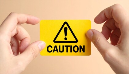 Hands holding yellow “CAUTION” card with black triangle and exclamation mark
