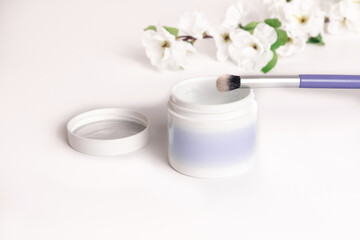 Skincare product alongside brush with white flowers in the background during a natural light setting