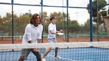  adult man paddle tennis player during friendly doubles pair match with guy partner at outdoors court. High quality 4k footage - Powered by Adobe