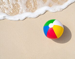 Obraz premium Colorful Beach Ball near Ocean Foam: Toy Resting on Wet Sand Close to Rolling Sea Wave with Playful Vibe, Summer Atmosphere, and Coastal Scene on Sunny Shoreline for Holiday Concept