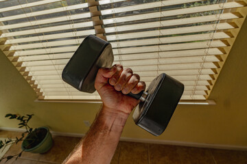 Arm Holding a Dumbbell Against a Sunny Window with Blinds