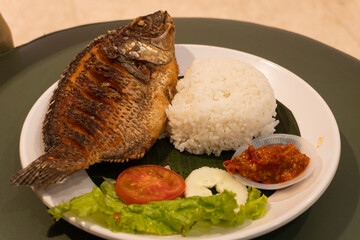 Delicious fried fish with rice, cucumber, lettuce, tomato with Indonesian spicy chili sauce.