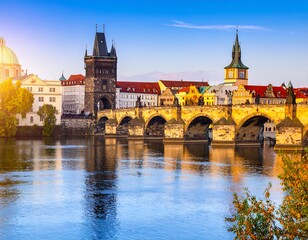 Fototapeta premium Prague's Charles Bridge at sunrise. Golden light bathes the stone bridge, reflecting on the still river. Towers and colorful buildings line the opposite shore