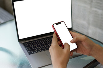 Hands holding a smartphone with a blank screen in front of an open laptop. Multi-device mockup for responsive website or app design presentation.