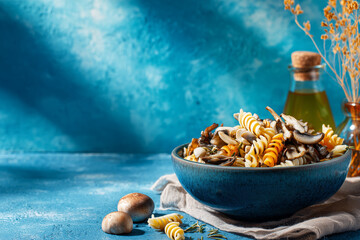 Pasta Dish with Mushrooms. Pasta with mushrooms in a blue bowl on a rustic table. Ideal for culinary blogs or recipe websites.