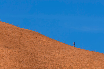 Athletic man with his face covered by a net to protect himself from insects, on top of an orange rock, Australia