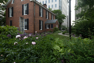 Historic brick building surrounded by vibrant garden in urban setting on a cloudy day