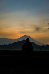 Fototapeta premium Solitary figure silhouetted against mountain sunset