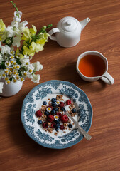 Natural yogurt with crispy granola, raspberries and blueberries on a wooden table, top view. Delicious breakfast