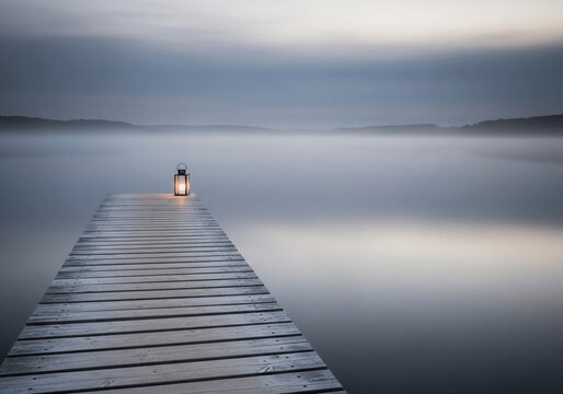 Fototapeta Lantern on wooden pier over misty lake