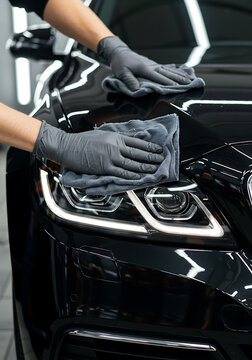 Headlight of dark luxury car cleaned gently with cloth by professional in auto detailing shop