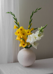 A bouquet of yellow and white gladioli in a round ceramic vase on the living room table