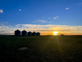 Grain bins and silos with farm equipment blue skies and montana wheat fields at sunset 