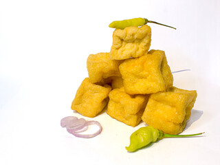 Golden fried tofu pyramid with fresh green chilies and red onion slices on a clean white background. Perfect for Indonesian street food, vegan, or spicy cuisine themes.