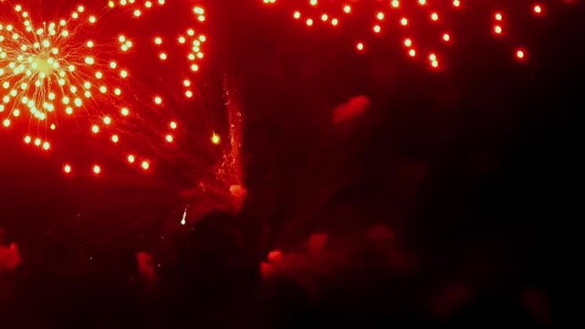 Vibrant red fireworks explode and spread across the inky night. The bursts create a luminous glow, painting the sky with fiery patterns during an outdoor Summer celebration.