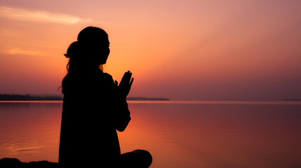 silhouette of woman praying at sunset. radiant orange and purple sky reflected in tranquil water. serene and spiritual atmosphere.