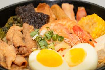A hearty bowl of seafood noodle soup filled with shrimp, corn, egg, vegetables, rice blood cake, tofu skin, and assorted hotpot ingredients. The colorful ingredients float in a rich broth, making for 