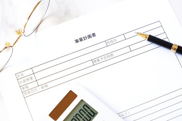 事業計画書 - 新規事業の立ち上げに先立ち、事業計画書を作成する起業家のイメージ
