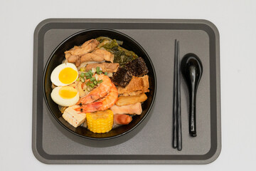 A hearty bowl of seafood noodle soup filled with shrimp, corn, egg, vegetables, rice blood cake, tofu skin, and assorted hotpot ingredients. The colorful ingredients float in a rich broth, making for 