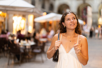 Young woman walks around Barcelona at night, she looks at restaurants and chooses which one to go to. Evening and nightlife in Barcelona
