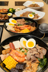 A hearty bowl of seafood noodle soup filled with shrimp, corn, egg, vegetables, rice blood cake, tofu skin, and assorted hotpot ingredients. The colorful ingredients float in a rich broth, making for 