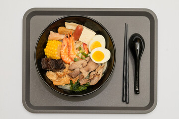 A hearty bowl of seafood noodle soup filled with shrimp, corn, egg, vegetables, rice blood cake, tofu skin, and assorted hotpot ingredients. The colorful ingredients float in a rich broth, making for 