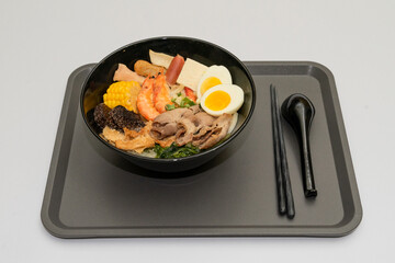 A hearty bowl of seafood noodle soup filled with shrimp, corn, egg, vegetables, rice blood cake, tofu skin, and assorted hotpot ingredients. The colorful ingredients float in a rich broth, making for 