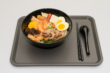 A hearty bowl of seafood noodle soup filled with shrimp, corn, egg, vegetables, rice blood cake, tofu skin, and assorted hotpot ingredients. The colorful ingredients float in a rich broth, making for 