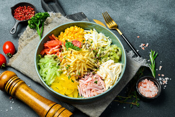 A plate of colorful vegetable salad made of cucumber, paprika, tomatoes, potatoes and boiled sausage. On a dark stone background.