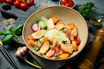 Caesar salad with chicken and vegetables. On a plate. Restaurant serving. Close up. On a dark stone background.