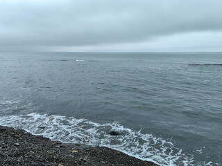 Overcast seashore with gentle waves, pebble beach, and a calm grey sea stretching to the horizon, peaceful and minimalistic coastal scene.